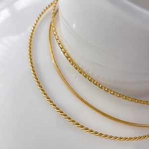 Macro detail of three gold metal bangles showing twisted rope and textured surface textures