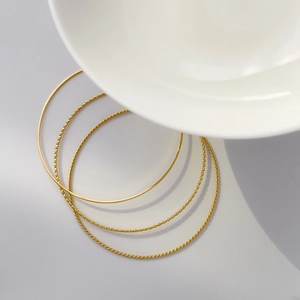 Detail of four-piece minimalist gold stackable bracelets with twisted and textured patterns