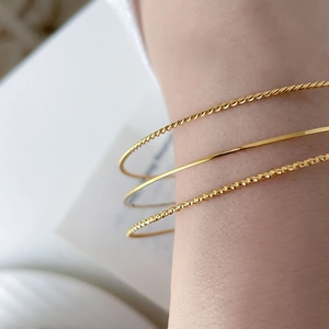 Close-up of three gold bracelets showing twisted rope and flat textures on a model wrist