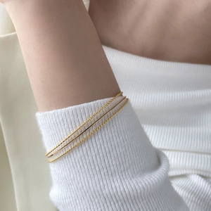 Detailed view of three minimalist gold-toned bracelets featuring twist and beaded textures