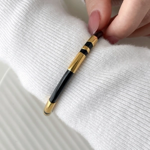 Detail of minimalist gold and black enamel twisted bangle on a white knit sweater sleeve
