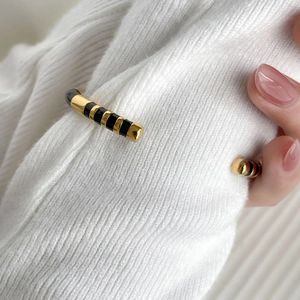 Detail of twisted gold bangle with black enamel stripes over white knit cuff