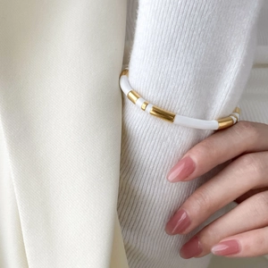 Detail of white enamel and gold beads bracelet styled over a white knit sleeve