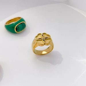 Detail of a gold signet ring with floral motif and green enamel clover ring on a white base