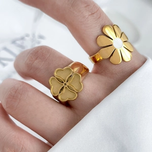 Detail view of gold clover and daisy rings set with white enamel and matte texture