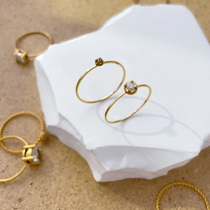 Detail of 18K gold plated twisted band rings with zircon inlay on a white stone display