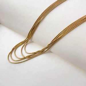 Detail of layered gold snake bone chains draped elegantly over a minimalist white prop