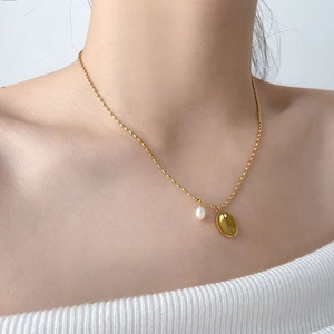 Close-up of a layered gold necklace featuring a freshwater pearl and oval pendant
