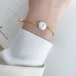 Detail of baroque pearl bracelet on wrist with gold stainless steel chain and oval tag