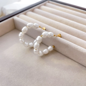 Detail of baroque pearl hoop earrings with 18K gold plated titanium on beige velvet