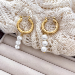 Detail of C-shaped 18K gold plated hoop earrings with three dangling white pearls