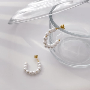 Detail view of gold C-shaped earrings with three pearls on a transparent glass display
