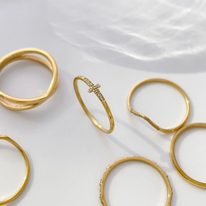 Detailaufnahme goldener Kreuz- und Wellenringe mit Zirkoniasteinen auf hellgrauem Hintergrund