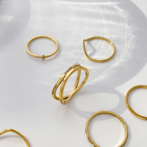 Detailansicht goldener Zirkon-Kreuzring und minimalistische Bänder unter Wasser-Lichteffekten
