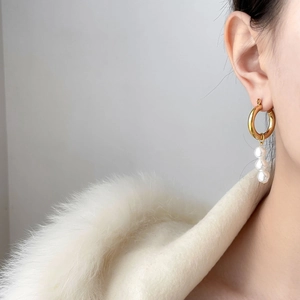 Close-up of elegant gold C-shape hoop earrings with three dangling white pearls