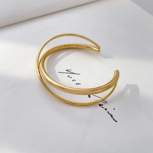 Close-up of triple-layered golden minimalist open bracelet with intersecting sleek lines