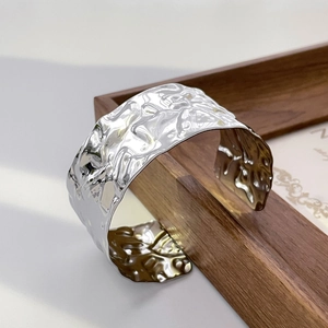 Macro shot of silver wide open cuff bracelet with irregular hammered texture on wood frame