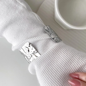 Macro shot of silver wide open cuff with irregular lava texture on white knit sleeve