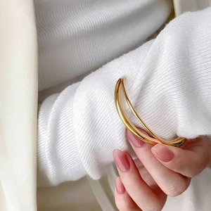 Polished double-layered gold bangle worn over white knit sweater and cream blazer