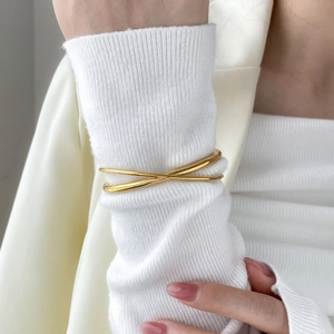 Minimalist 18K gold plated stainless steel crossover bangle worn over a sweater cuff