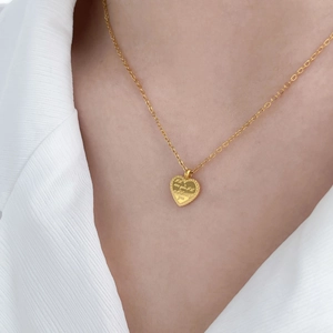 Gros plan du collier pendentif cœur plaqué or avec gravure sur un mannequin en blanc