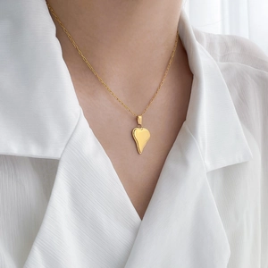 Gros plan d'un collier doré avec pendentif cœur irrégulier porté sur une chemise blanche
