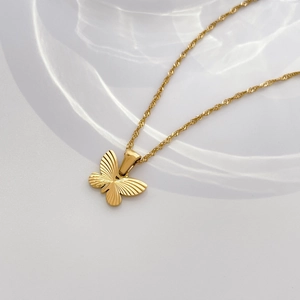 Détail du pendentif papillon doré avec texture nacrée sur une chaîne à vagues
