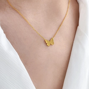 Gros plan d'un collier pendentif papillon doré porté sur un blazer blanc texturé