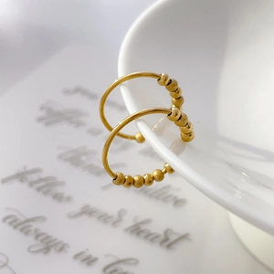 Macro shot of 18K gold plated titanium hoop earrings with delicate beaded charms on white porcelain