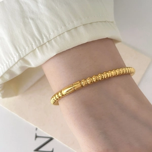 Detailed view of polished 18K gold plated bead bracelet on wrist with elegant shirt