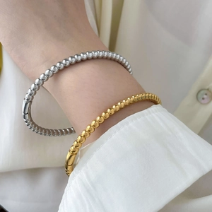 Detailed view of polished bead bangles in gold and silver finish on a wrist