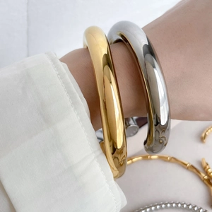 Close-up of chunky hollow curved bangles in polished gold and silver steel finish