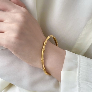 Detailed view of an 18K gold plated bamboo-style bangle on a wrist with a white shirt