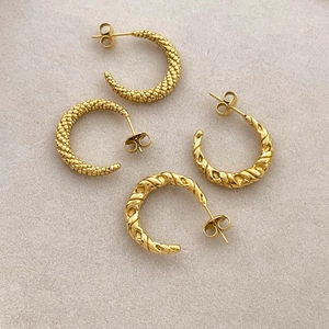 Macro detail of C-shaped twisted gold earrings with intricate horn and rope textures