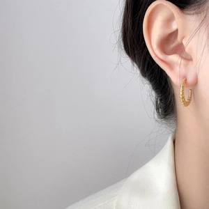 Golden C-shaped twisted earrings with horn texture shown on a model in a white blazer