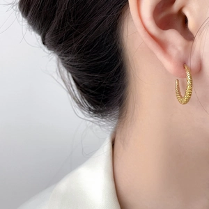 Detailed close-up of 18K gold plated C-shaped earrings with unique twisted rope texture