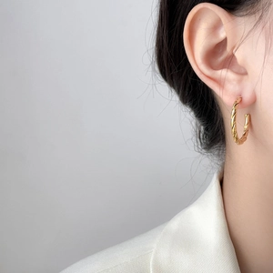 Close-up of a model wearing C-shaped twisted rope earrings in 18K gold plated steel