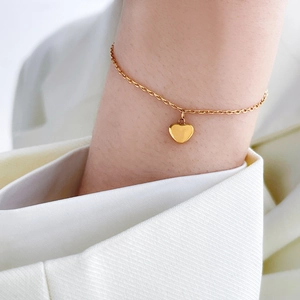 Detailed view of a gold titanium bracelet with a heart pendant on a model's wrist