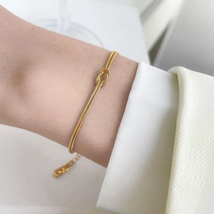 Detailed close-up of a golden double-layered snake chain bracelet with a knot design
