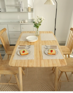 Detail showing four light beige linen placemats on a minimalist wooden dining table setup