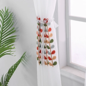 White sheer curtain with colorful leaf embroidery and a decorative floral tieback