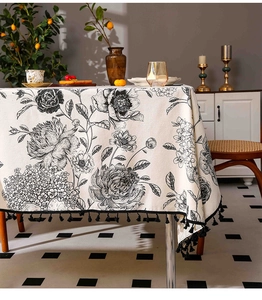 Close-up of linen tablecloth with black floral prints and decorative tassel fringe