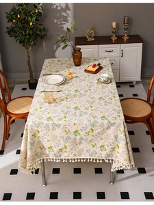 Detail of floral linen tablecloth with beige tassels on a rustic wooden dining table
