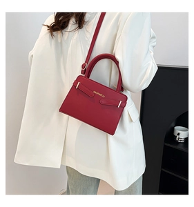 Gros plan du sac à main trapèze bordeaux avec logo doré et finitions métalliques chic