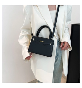Détail d'un sac à main noir en simili cuir avec boucle dorée porté par un mannequin