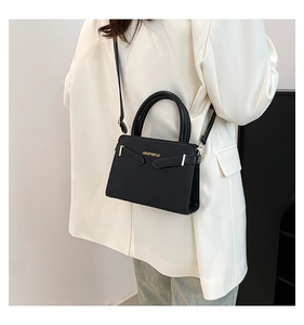 Détail d'un sac à main structuré en cuir noir avec logo doré et bandoulière fine