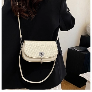 Détail du sac selle beige tissé avec fermoir rotatif métallique et bandoulière réglable