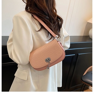 Détail du sac à bandoulière tressé rose avec fermoir rotatif argenté sur un costume blanc