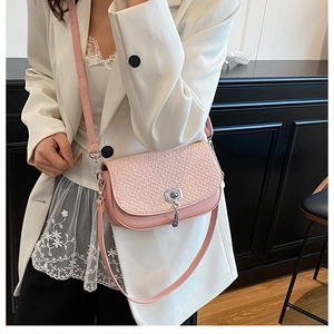 Détail du sac selle tissé rose clair avec fermoir argenté sur un tailleur blanc chic