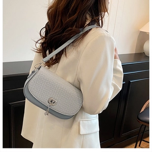Gros plan d'un sac selle bleu clair tissé avec fermoir argenté sur blazer blanc